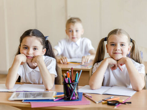 Children sitting in a school classroom with their exercise books open.